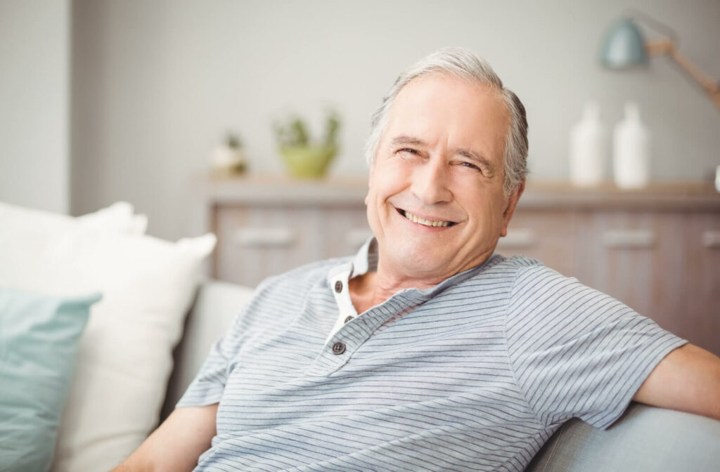 A senior man smiling looking directly and sitting on a couch.