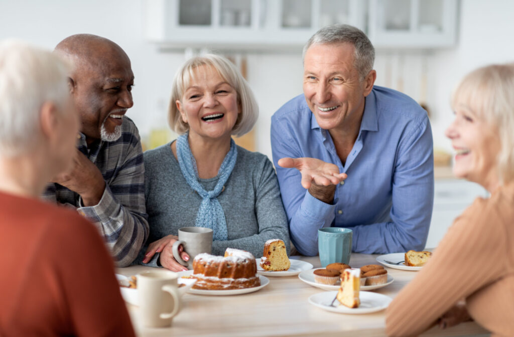A group of seniors sitting around a table, eating and enjoying afternoon tea and cake, while smiling and chatting with each other.