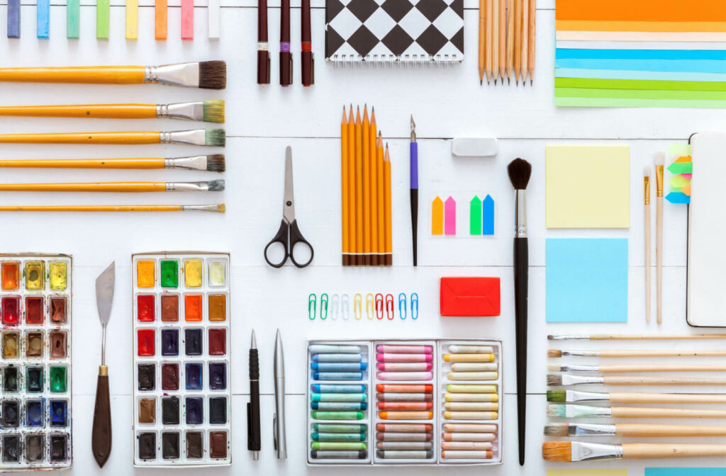 Top view of art supplies arranged on a desk, including creative tools such as drawing and painting stationery, color paints, brushes, pencils, and crayon