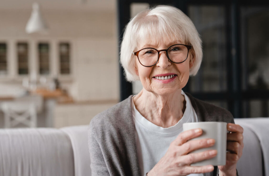 A happy senior woman enjoying a hot beverage in her living room.