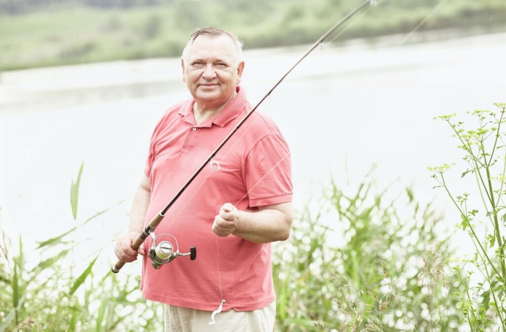 An older adult man holding a fishing rod, smiling and looking directly at the camera